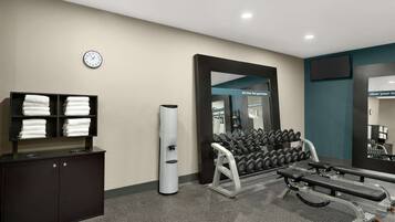 Une salle de sport équipée d’un banc de développé couché, d’haltères, d’un porte-serviettes et d’une horloge au mur.