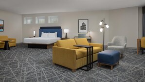 A hotel room with a bed, a sofa, a chair, a small table, and a floor lamp. - Hampton Inn & Suites Exeter (Exeter)