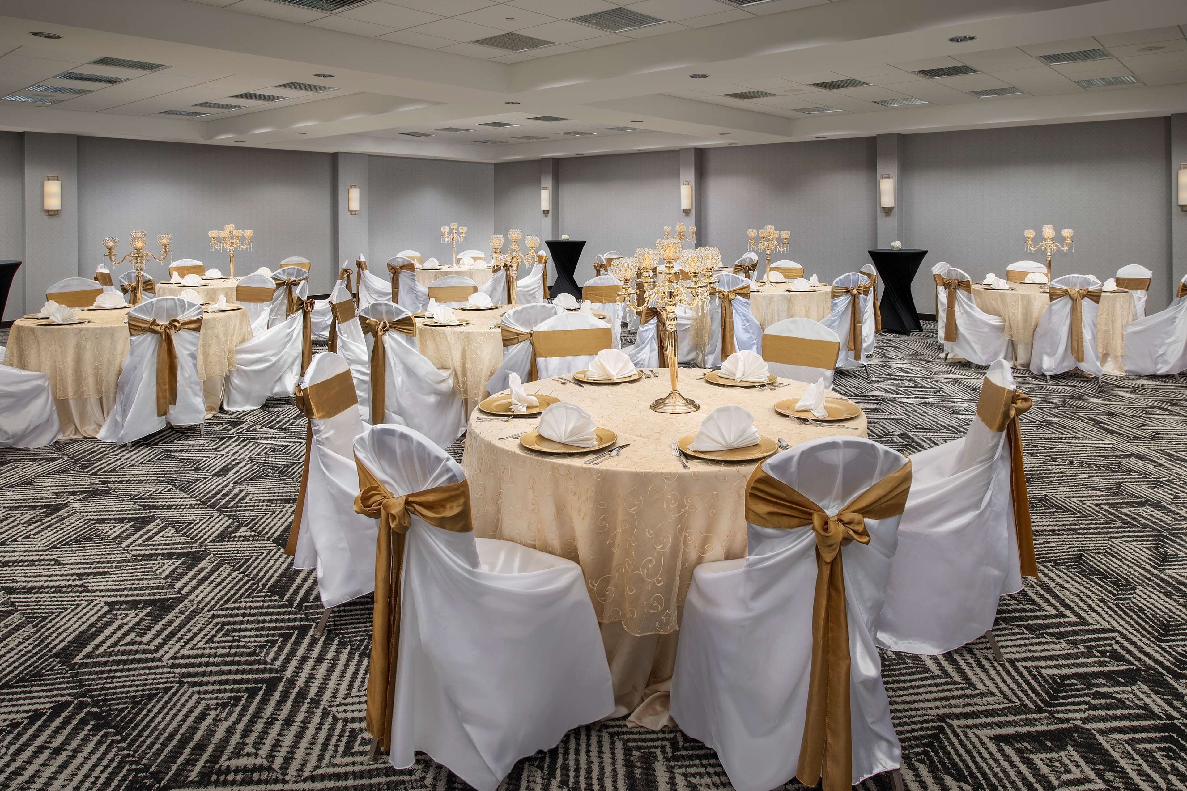 Un salón de banquetes con mesas redondas, sillas blancas y doradas, y candelabros.