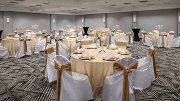 Un salón de banquetes con mesas redondas, sillas blancas y doradas, y candelabros.