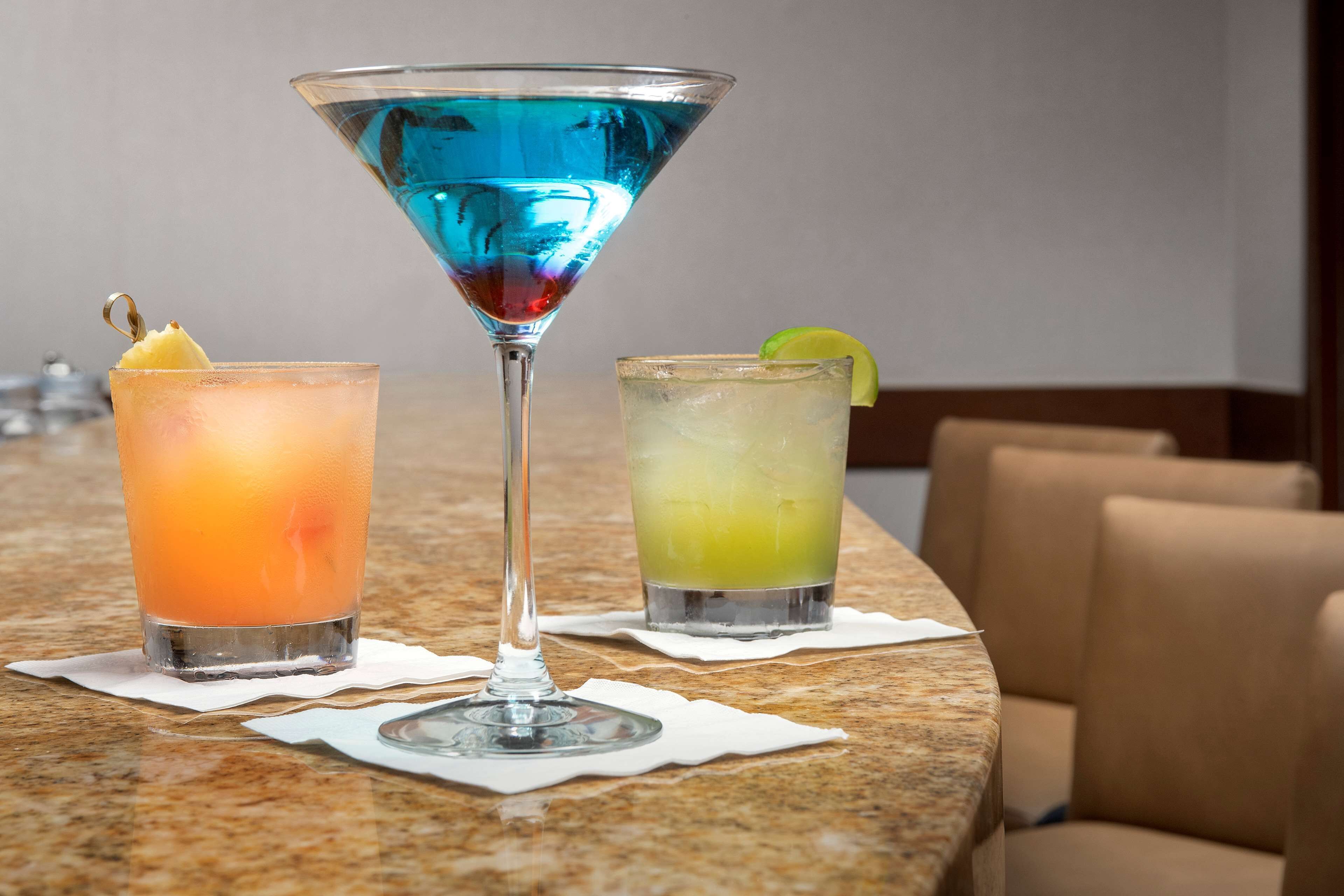 Três cocktails sobre um balcão de mármore com guardanapos.