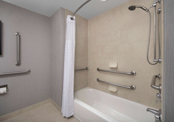 A modern bathroom with a bathtub, shower, grab bars, and a towel rack.