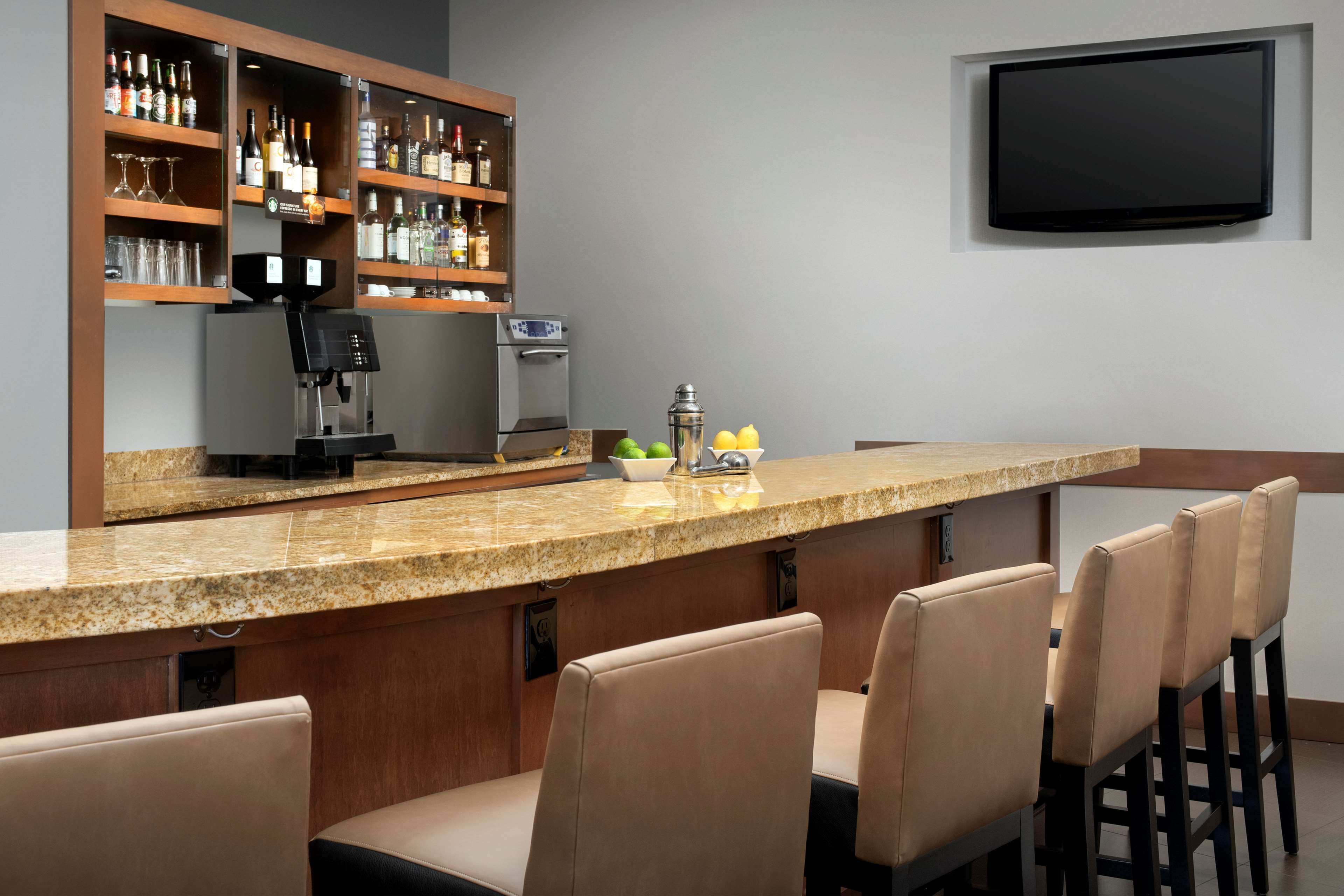 A bar area with a granite countertop, bar stools, a coffee machine, and a shelf with bottles and glasses.