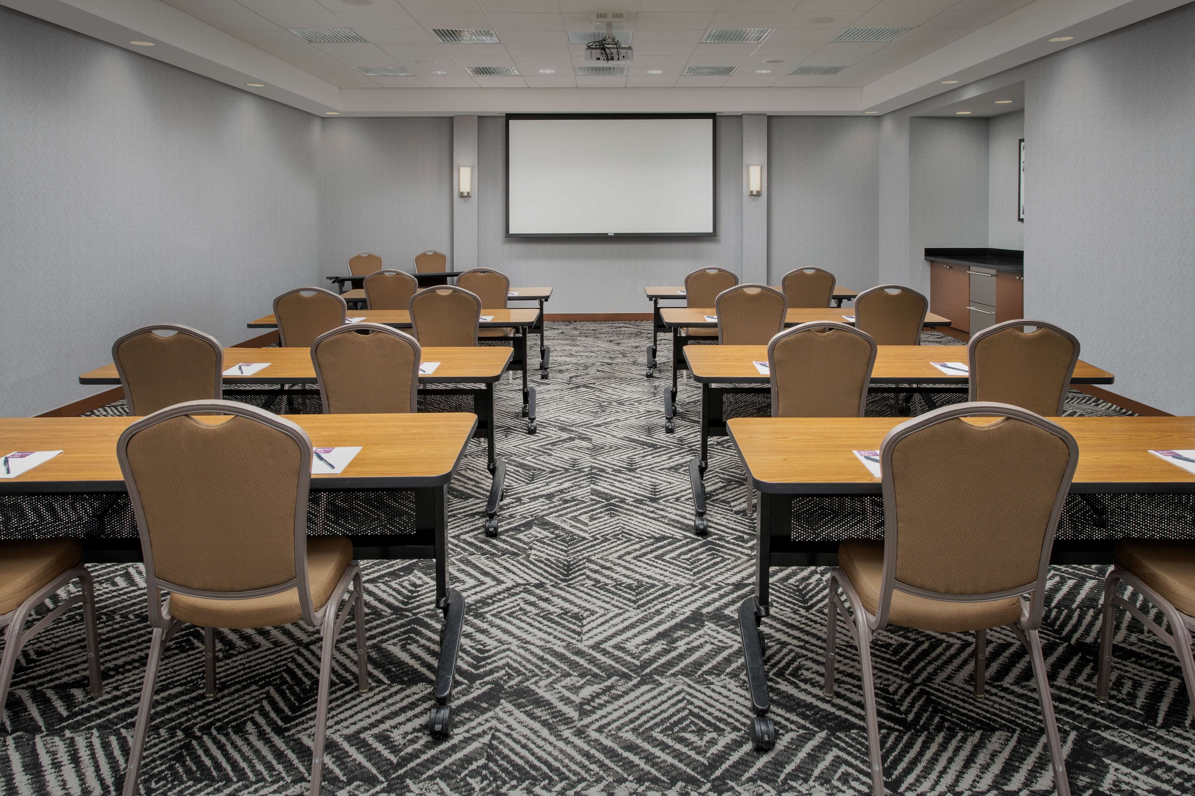 A conference room with a large screen, multiple tables, and chairs.