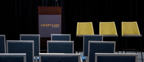 A conference room with a podium labeled "COURTYARD BY MARRIOTT," blue chairs, and yellow chairs.