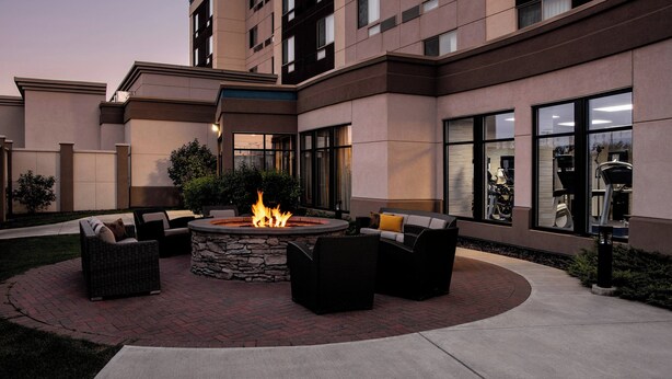 A courtyard with a fire pit surrounded by outdoor furniture, a stone wall, and a building with large windows and balconies. - Courtyard by Marriott Edmonton West (Edmonton)