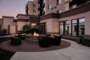 A courtyard with a fire pit surrounded by outdoor furniture, a stone wall, and a building with large windows and balconies. - Courtyard by Marriott Edmonton West (Edmonton)