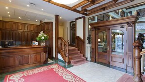 Un vestíbulo con paneles de madera, un mostrador de recepción, una escalera y una araña.