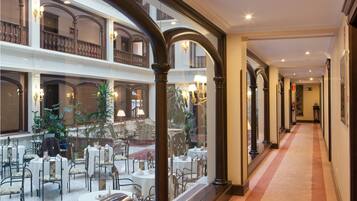 A hotel lobby with a central open space, multiple dining tables, and a view of the upper floor balcony.