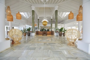 Un hall d’entrée spacieux avec un comptoir d’accueil, des fauteuils en osier et un sol en marbre.