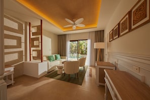 A modern hotel room with a ceiling fan, a sofa with green cushions, a dining table, and a view of the outdoors.