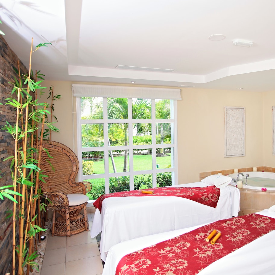 A hotel room with two beds, a sitting area, a bathtub, and a view of the outdoors.