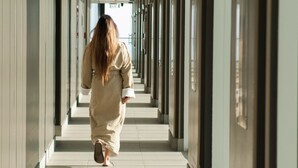 Un pasillo con una persona alejándose, con varias puertas y ventanas.
