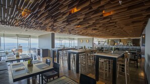 Un restaurante moderno con un diseño de techo único, amplias ventanas que ofrecen vistas al océano y un comedor espacioso con varias mesas y sillas.