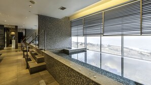 Un área de piscina interior moderna con vistas a la costa, una pared de azulejos y una escalera que lleva a un nivel superior.