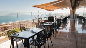 Una terraza con mesas y sillas, con vista al mar y edificios.