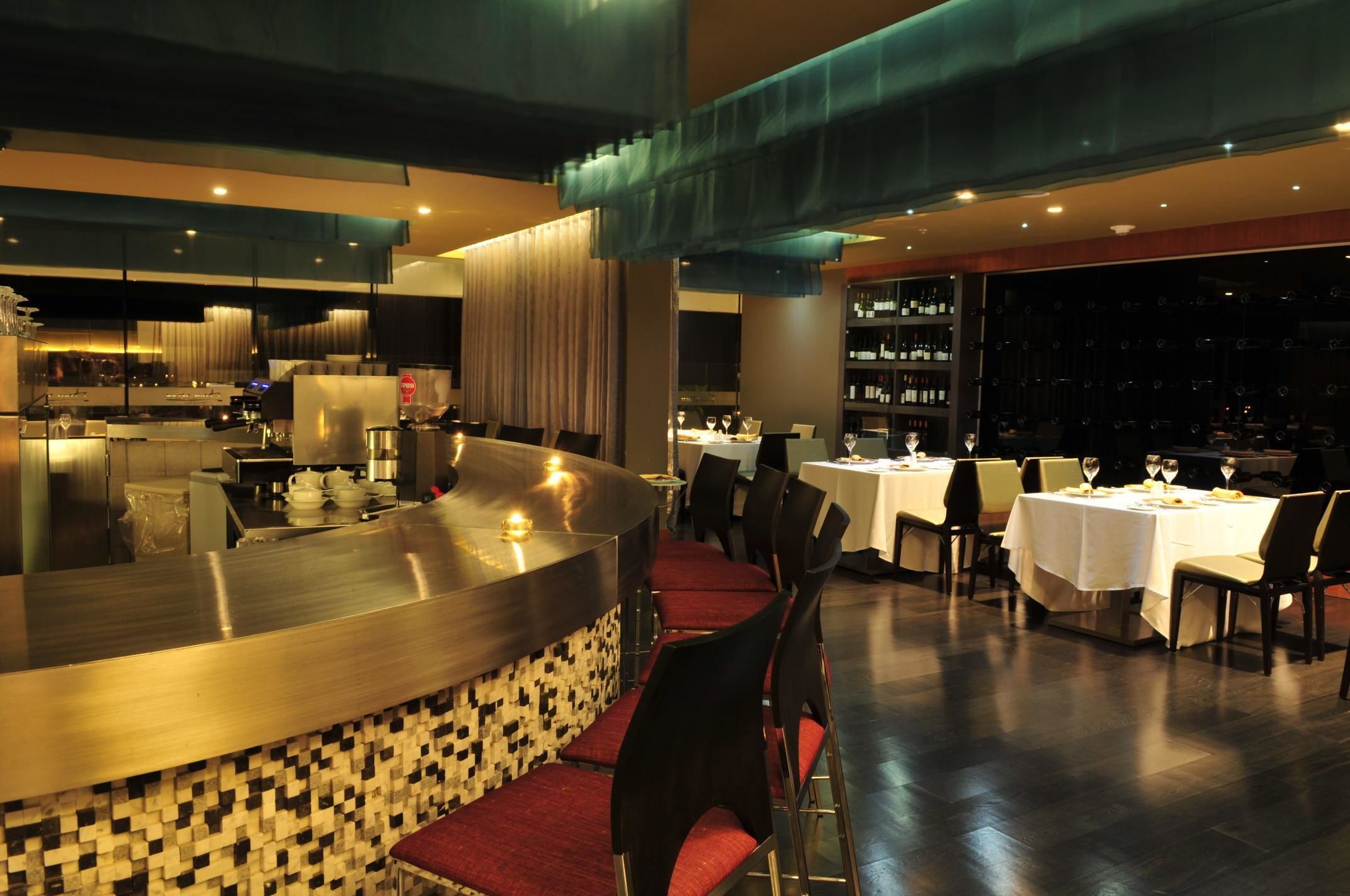 A modern restaurant with a bar area, dining tables, and a wine display.