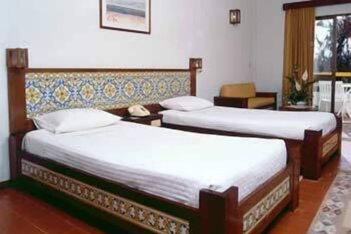 A hotel room with two single beds, a small table, a chair, and a window with curtains.