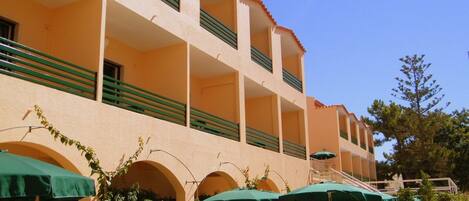 Un hotel con terraza exterior, toldos verdes y una escalera que lleva a los pisos superiores.
