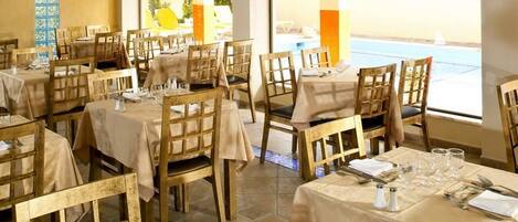 A dining area with tables set for service, chairs, and a view of the sea.