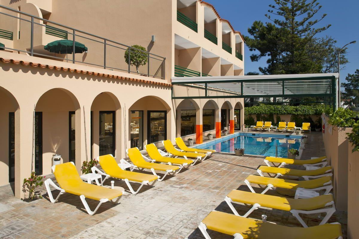 Un área junto a la piscina con sillas reclinables amarillas, una pileta y un espacio de descanso cubierto con techo de vidrio.