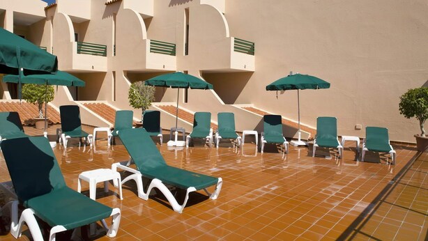 A sunlit outdoor lounge area with multiple green umbrellas and white lounge chairs arranged on a tiled floor. - Casablanca (Vila Real Santo Antonio)