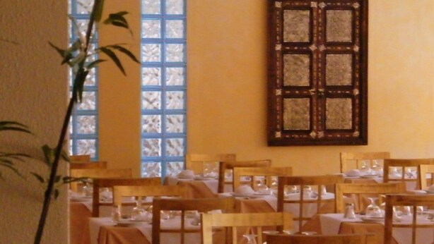 A dining area with tables set for service, a large window with blue panes, and a decorative wooden panel on the wall. - Casablanca (Vila Real Santo Antonio)