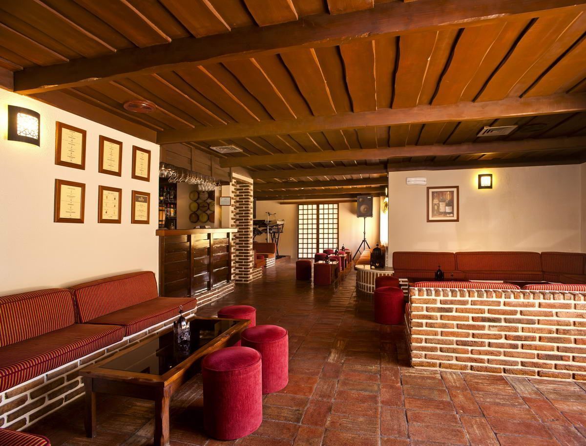 A cozy lounge area with a brick wall, wooden ceiling, and red upholstered seating.