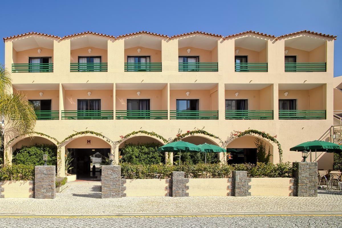 Ein mehrstöckiges Hotel mit Balkonen, einem zentralen Eingang und Außenbereich-Sitzgelegenheiten.