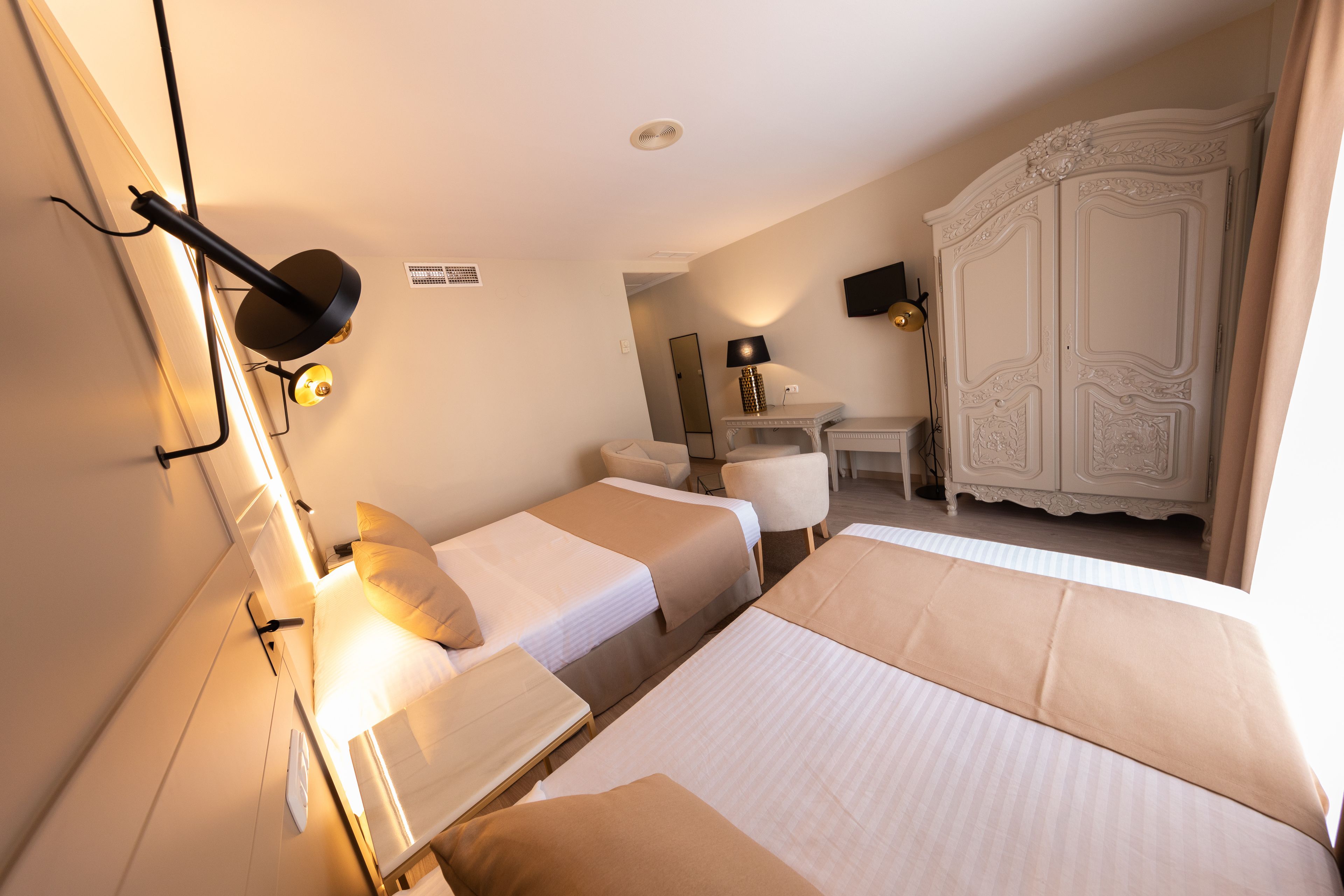 A hotel room with two beds, a desk, a chair, a wardrobe, and a lamp.