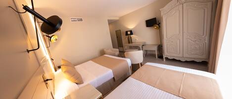 A hotel room with two beds, a desk, a chair, a wardrobe, and a lamp.