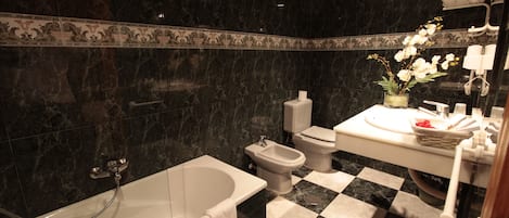 A bathroom with a checkered floor, a bathtub, bidet, toilet, and a sink with a vase of flowers.
