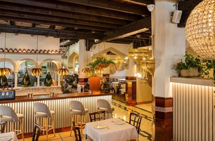 Un interior de restaurante con una zona de bar, varias lámparas colgantes y diferentes opciones de asientos.