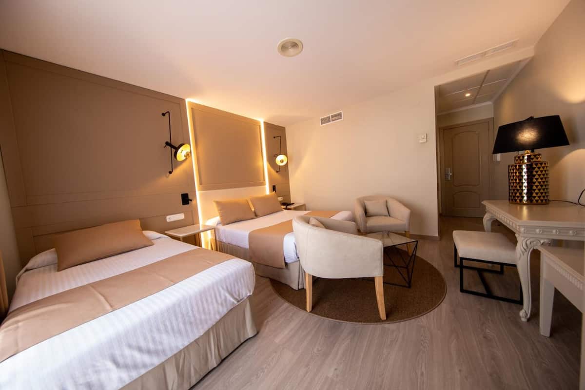Una habitación de hotel con dos camas, un escritorio, una silla y una lámpara.
