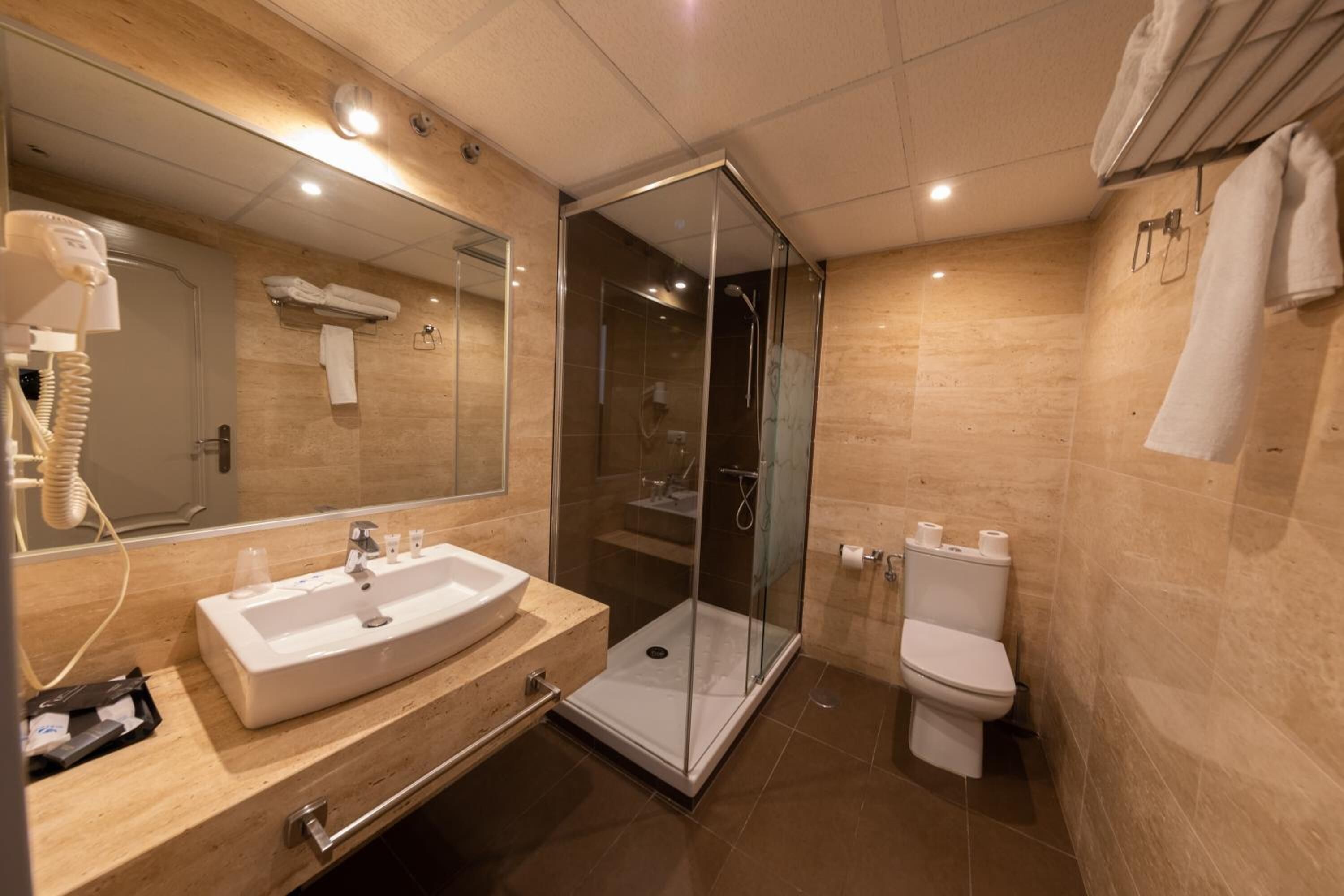 Un baño moderno con ducha de vidrio, lavamanos con espejo y retrete.