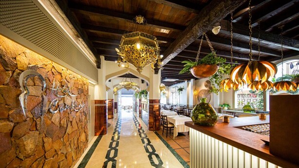 A restaurant interior with a stone wall, a patterned floor, hanging plants, and a wooden ceiling. - Hotel Casablanca (Almunecar)