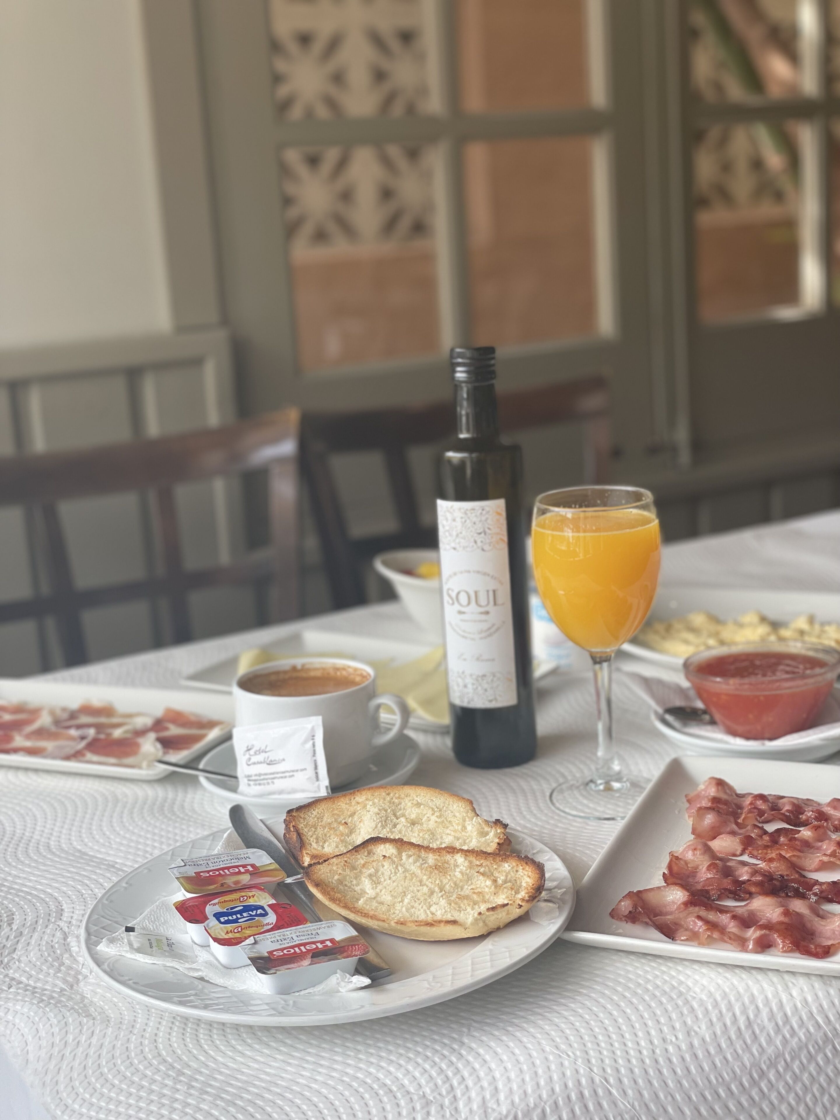 Et morgenbord med croissanter, bacon, en vinflaske, et glas appelsinjuice og en kop kaffe.
