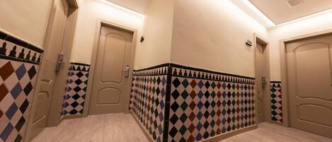 Un pasillo de hotel con suelo de estampado ajedrezado, paredes color beige y puertas.