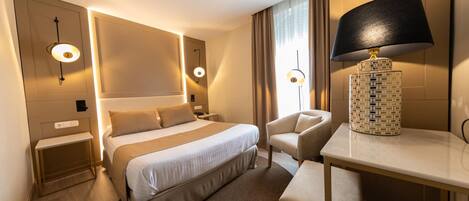 A hotel room with a large bed, bedside tables, a desk with a lamp, and a chair.