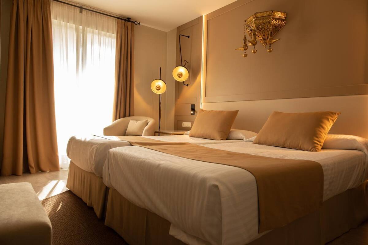 Una habitación de hotel con una cama grande, dos mesitas de noche, una silla y una lámpara de pared decorativa.