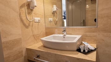 Un baño con lavamanos blanco, un espejo y un secador de pelo en la pared.