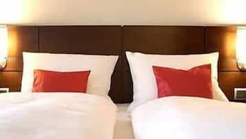 Habitación de hotel con dos camas, cada una con ropa blanca y almohadas rojas.