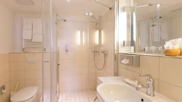 Un baño moderno con ducha de vidrio, lavamanos blanco y un espejo grande.