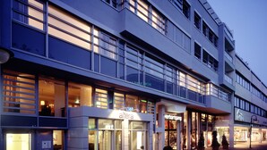 A hotel with a modern facade, multiple floors, and a variety of shops on the ground level. - Altera Hotel im Herbartgang (Oldenburg)