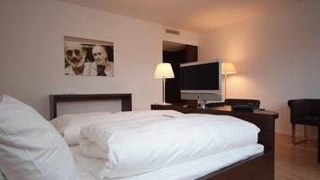 Una habitación de hotel con una cama, televisión, escritorio con lámpara y una silla.