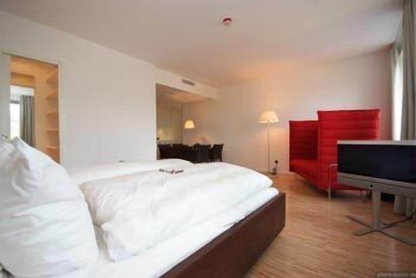 A hotel room with a large bed, a red armchair, a TV, and a desk.