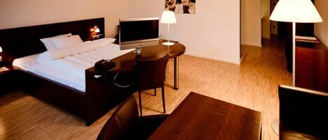 Una habitación de hotel con cama, escritorio, silla, lámpara y televisor.