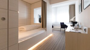 A modern hotel room with a bed, a desk, a chair, and a large window with curtains. - Altera Hotel im Herbartgang (Oldenburg)