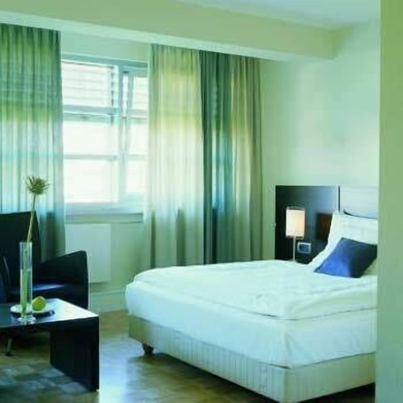 A hotel room with a bed, a desk, a chair, and a window with curtains.