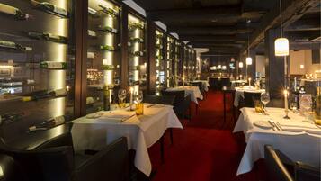A restaurant with multiple tables, each set with white tablecloths, wine glasses, and bottles.